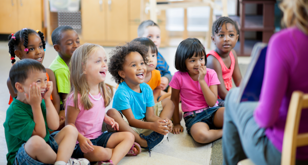 children sitting on the ground while teacher reads aloud