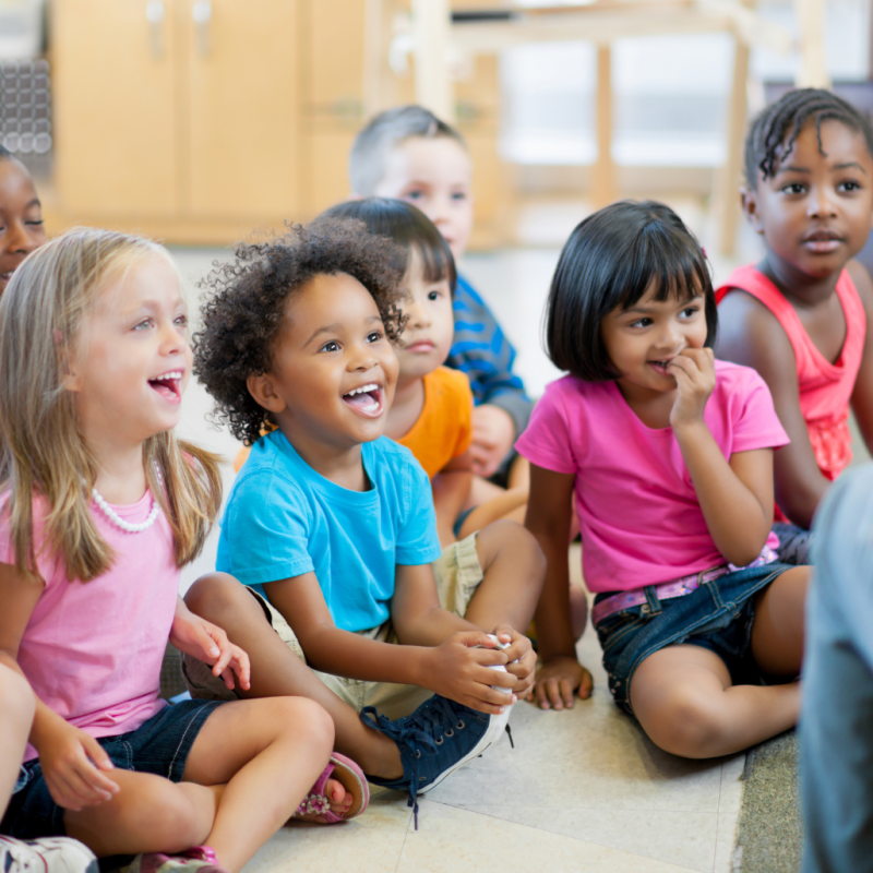 children sitting on the ground while teacher reads aloud