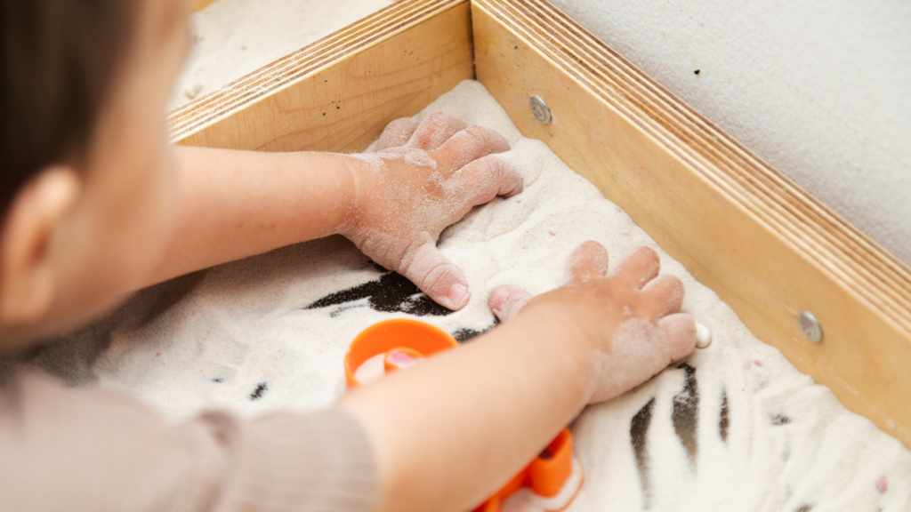 toddler playing in sand bin