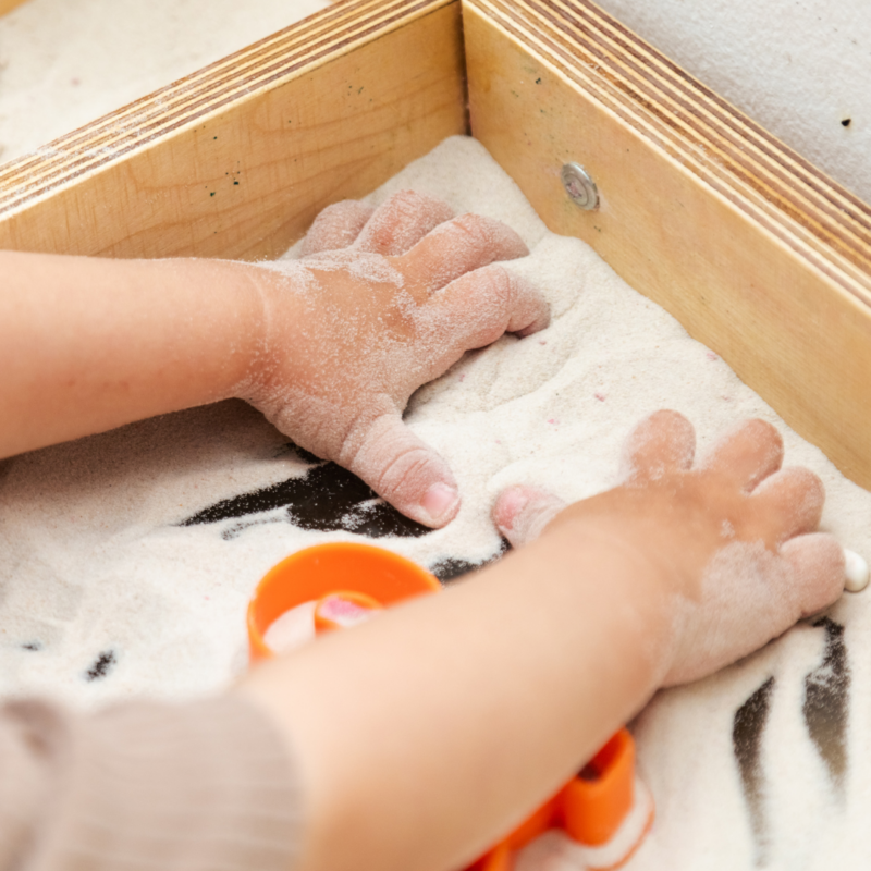 toddler playing in sand bin